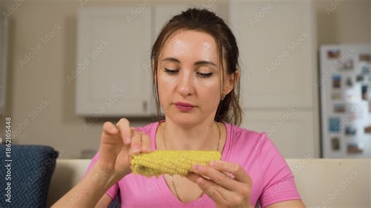 Woman sprinkling salt on corn cob before eating. Girl adding seasoning to maize before bite. Female salting sweetcorn and continuing meal at dining table