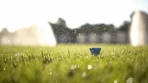 Golf club hits a golf ball in a super slow motion. Drops of morning dew and grass particles rise into the air after the impact. | Premium Stock Video Footage