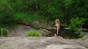 Barefoot woman hikes on mountain trail by rocky river. Female hiker enjoys nature, tranquil scenery, freedom outdoors. Wellness hike, natural terrain adventure, eco tourism in rich landscape. Slowmo