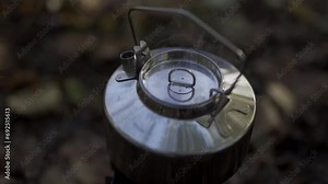 The hand of a person making tea in an old fashioned wood stove kettle in the woods