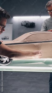 Two male automotive designers creating futuristic plasticine clay model of car with professional tools. Future design of new generation electric car. Working in modern car design studio. Vertical