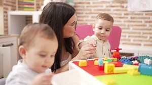 Teacher with boys playing with construction blocks sitting on table at kindergarten