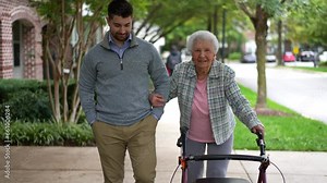 Grandmother using a walker and grandson smiling and walking together outside.