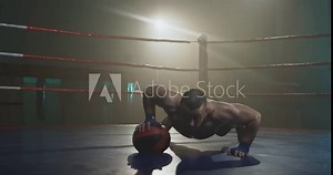 Caucasian sweaty strong man pushing up on one arm and ball at boxer ring in darkness. Sportsman doing push ups and changing hands. Boxer warming up.