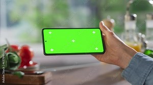 Anonymous Woman Using Smartphone with Mock Up Green Screen Chromakey Display on Kitchen Table With Utensils and Food Ingredients. Female Watching Horizontal Cooking Recipe Video Tutorial