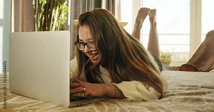 Cute girl with laptop laughing. Laughing girl messeging, chatting with friends online. Girl posting photos and videos, reading and commenting on friends posts, and laughing at funny memes and jokes