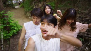 Group of Young Asian man and woman enjoy outdoor lifestyle travel nature forest on summer holiday vacation. Happy generation z people friends using mobile phone vlogging together at waterfall lagoon.