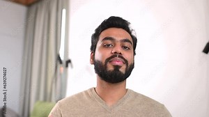 Portrait of happy young Indian guy sitting at desk and gesturing. Smiling ethnic man involved virtual meeting. Hispanic male student taking a part in educational conference