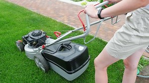 A woman starts a lawn mower. Mowing green grass. Side and top view.