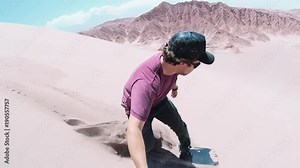 Young man sandboarding over great Sand Dunes of the Dead Valley, Atacama desert. Man using an action camera when slide on a sandboard.