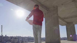 Architect looks at the floor plan, standing on the last floor of the high-rise office building under construction. Backlight