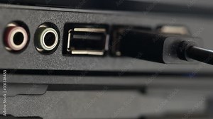 USB cable is inserted into socket. Black panel with colored connectors for microphone and headphones, and also Universal Serial Bus connection ports close-up. Macro of hand inserting black cable