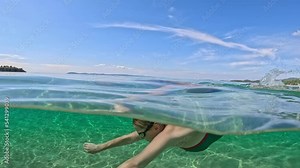 Young woman dives and swims in clear sea water. Girl swimmer in green swimsuit underwater at sea. Half underwater slow-motion shot
