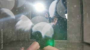 A young dancer performs a contemporary dance under the water rain in studio. A dancer girl dancing active dance in water with splashes in the beam of a spotlight