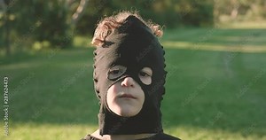close up of a young boy wearing a homemade ninja mask making facial expressions, no expression then smile then gritted teeth grimace or grin, in a park in the afternoon golden glow of the setting sun