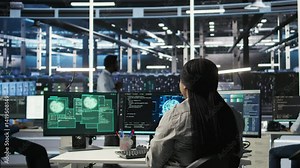 Server farm IT expert responds to security breach alert displayed on computer monitor, working to secure hardware. Data center employee attempts to protect equipment during cyberattack, camera A