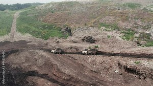 Aerial top view of a huge waste, garbage, dump, rubbish landfill. A landfill compactor sort out the garbage in the landfill. Trash trucks dump waste polluting products riding through the landfill.