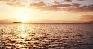 Aerial view flying over ocean into sunset, flying over water into beautiful sunset
