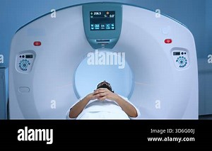 Magnetic resonance imaging computerized axial tomography. Patient finishing magnetic resonance procedure, sitting at moving scanner bed and looking at camera. Healthcare and cancer treatment.