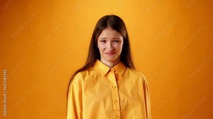 Teen girl showing disgusted grimace against orange background in studio