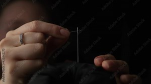 slow motion shot of thread passing through sewing needle. woman sewing project by hand. handmade fashion with quality thread and fabric. DIY and beautiful quilting by fashion designer. dark background