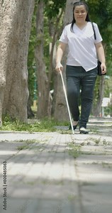 Woman with blindness disability walking on sidewalk contain tactile paving guide blocks using long white cane or blind cane a mobility tool to detect objects in the path for vision impairment people.
