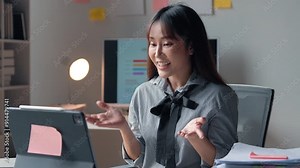 Confident professional woman in modern office engaging in remote video call. Utilizing tablet, surrounded by office supplies. Active and communicative