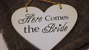 Slow moving shot of a heart shaped sign 'here comes the bride' in mixture of different fonts. The sign is led on a brown rug waiting to be hung up on the big day, filmed days before during preparation Stock Video