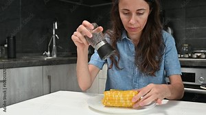 A woman salts corn on the cob and cooks it, which remains on a plate. Healthy vegetarian food concept