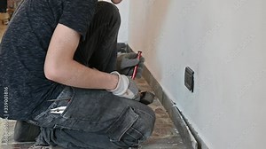 Masonry work in the apartment: a Caucasian boy is wearing work gloves and is using hammer and chisel to demolish the old baseboard. Close up on hammer.