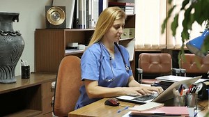 Positive woman doctor working in cabinet on laptop at workplace in medical office. High quality 4k footage