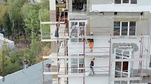 Workers stand on falsework and make thermoinsulation of wall