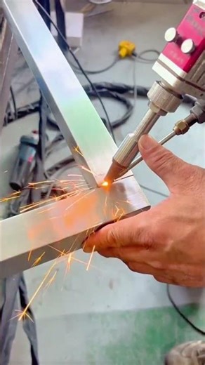 welding together shiny rectangular metal tubes using a precision laser machine with orange sparks