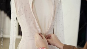 Unrecognizable female tailor fasten foundation garment on sparkling wedding dress on mannequin in bright studio. Close up of woman's hands zipping up the dress on the back