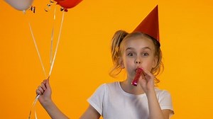 Joyful b-day girl with balloons using party blower and laughing on camera, fun