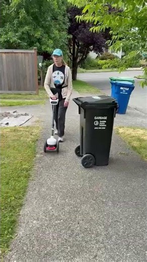 Glide, an AI mobility device guides Sheri, a blind user, around a trash can on a sidewalk.