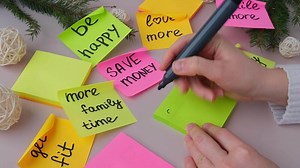 Female hands writing 2025 GOALS handwritten new year resolutions aims goals on sticky notes. Preparation for New Year. Concept of planning and setting goals for personal development