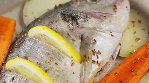 Dorado fish on baking sheet with vegetables, lemon and spices. Tilt down camera movement