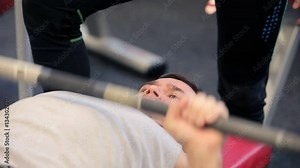 Bodybuilder. lfting. Paurlifting. The trainer insures the sports man. Gym. The man lifts heavy weight lying on a back. Training. The man does exercises. Bodybuilder lifting heavy barbell weights