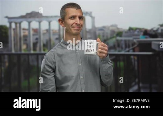 Man outdoors holding coffee cup with 'i am the boss' text, smiling confidently against historic city backdrop, showcasing empowerment and relaxation in a casual outdoor setting Stock Video Footage - Alamy