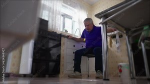 Elderly man suffering heart attack falling on floor needing medical emergency at home by kitchen sink. Sickly senior person experiencing cardiovascular pain