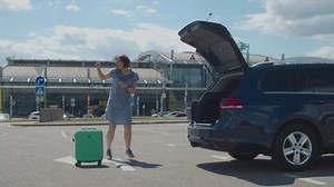 Young happy woman dancing alone with suitcase near airport building. Female tourist is happy to travel. Excited lady jumping and dancing.