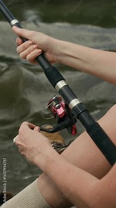 Unrecognizable woman sitting on coast, holding fishing rod and watching water for signs of movements