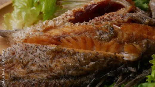 Whole deep fried sea bass barramundi with crispy golden skin served on fresh green lettuce leaves on round wooden plate