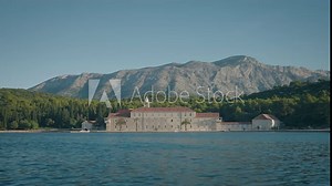 The view of Franciscan monastery from the blue sea on a sunny summer day. Visiting Badija island in Korcula. Beautiful mountains in the background.