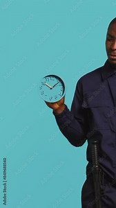 Vertical video Security guard holding clock, rushing people out of property. Portrait of stern bodyguard showing visitors time is passing, preparing for closing down location, studio background