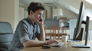 A young man talking on the phone working on the computer - Free Stock Video