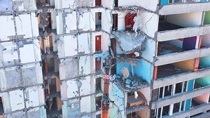 Demolishing machine breaks the walls and floors of the big ruined building. Aerial view of the deconstruction site.