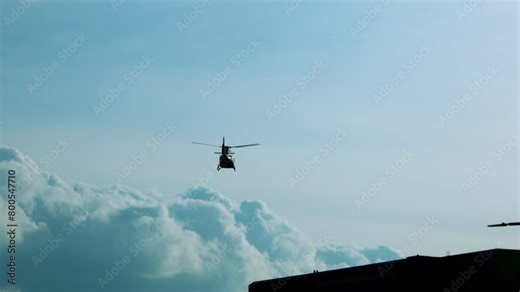 Low angle footage of silhouette helicopter hovering over building in cloudy sky during daytime