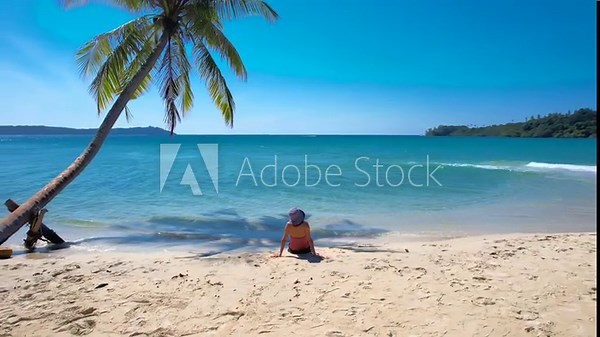 Rear view of young woman traveler sitting outdoors peacefully on the sand.